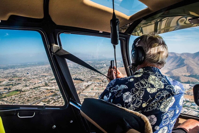 A person in a helicopter cockpit with a view of a city and mountains. 2