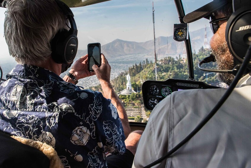 A person in a helicopter cockpit taking a photo with a smartphone. 4