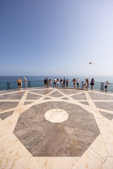 A group of people standing on a tiled platform overlooking the sea. 2