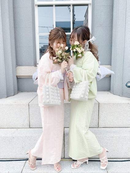 Two individuals holding bouquets in front of a building with large windows and a stone facade. 3
