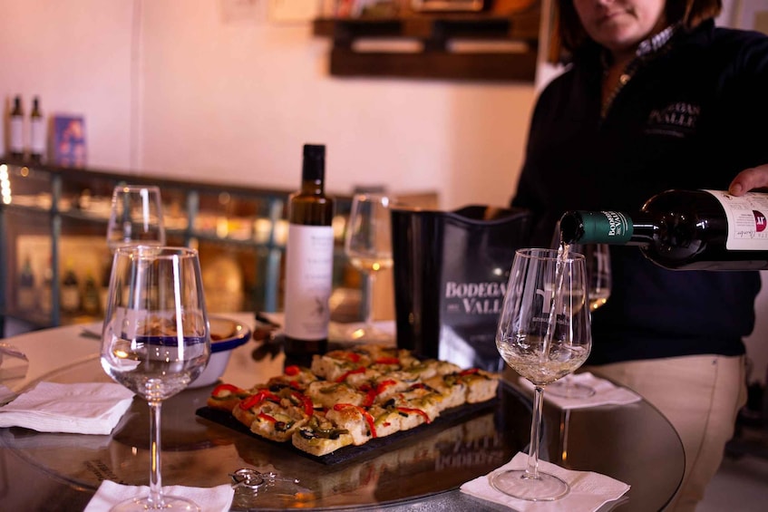 Una persona sirve vino en una copa, una botella de vino y un plato de comida sobre una mesa. 3