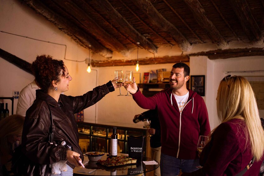 Un grupo de personas brindando con copas de vino en un entorno rústico con vigas de madera a la vista y una botella con la etiqueta 'BODEGAS VALLE' sobre una mesa. 5