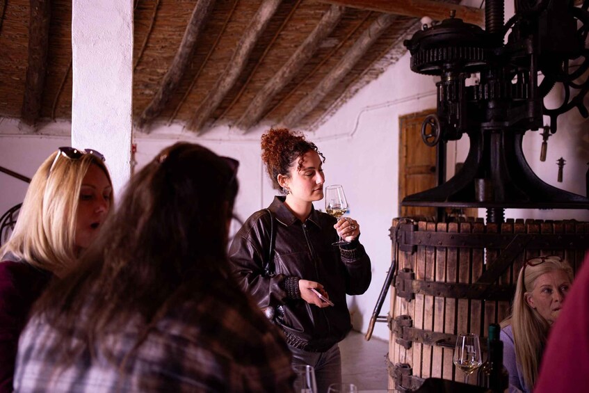 Un grupo de personas en una bodega rústica con vigas de madera y una gran prensa mecánica. 2