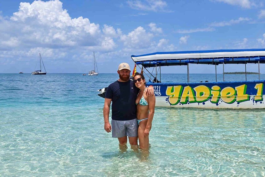 A couple standing in shallow water with a boat labeled 'YADIEL 1' in the background. 3