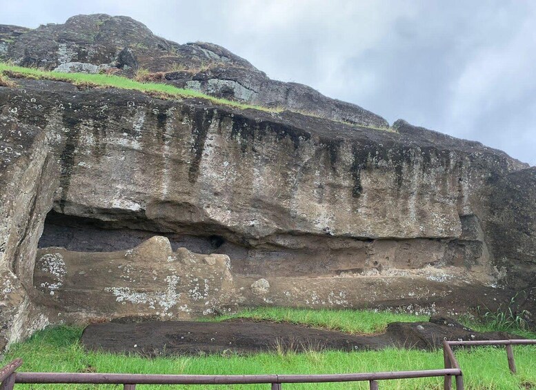 A large rock formation with a grassy foreground and a cloudy sky. 3