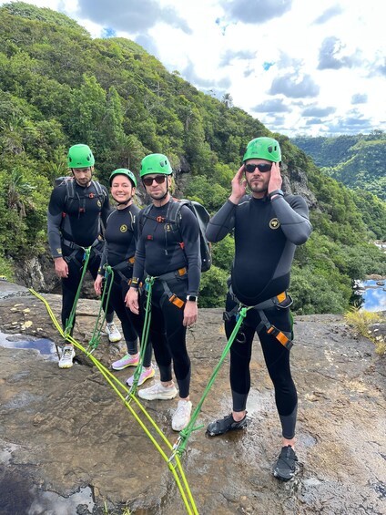 Four people in helmets and harnesses standing on a rocky outcrop with a mountainous landscape in the background. 5