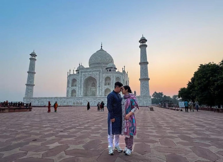 A couple standing in front of the Taj Mahal with its four minarets and large dome visible. 1