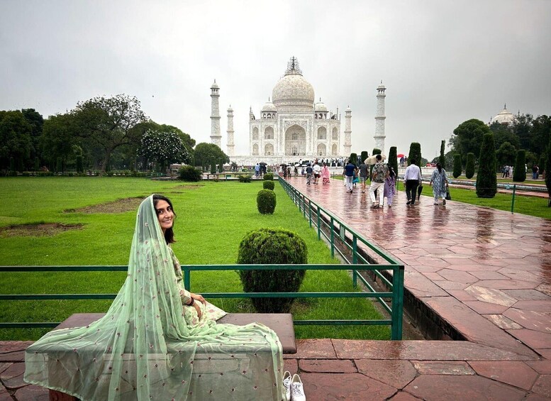 A person sitting on a bench in front of the Taj Mahal, with a green lawn and a pathway leading to the monument. 1