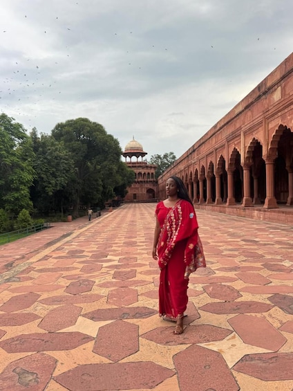 A woman in a red dress walking on a patterned stone floor with a large building in the background. 3