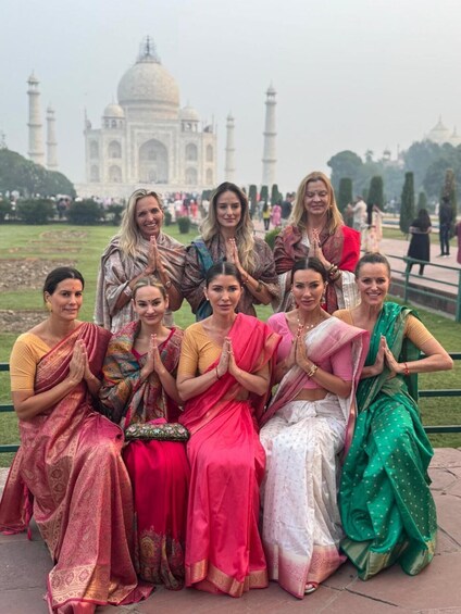 A group of women in traditional Indian attire sitting in front of the Taj Mahal. 4