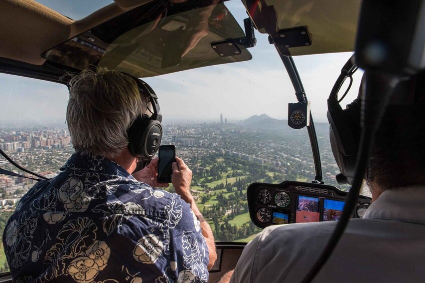 A person taking a photo from a helicopter cockpit with a cityscape in the background. 1