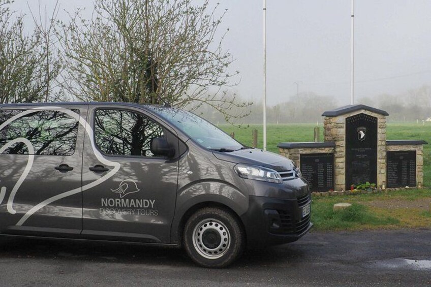 Una furgoneta gris con la marca 'Normandy Discovery Tours' estacionada en una calle. 2