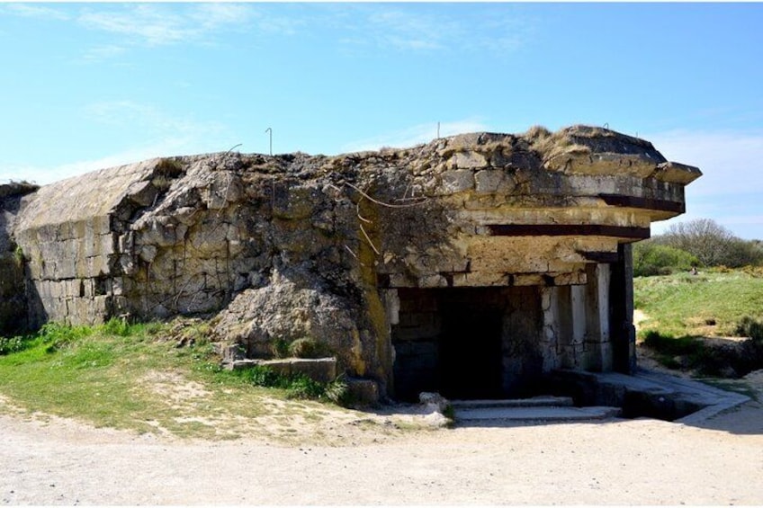 A stone structure with a doorway, surrounded by grass and a clear sky. 3
