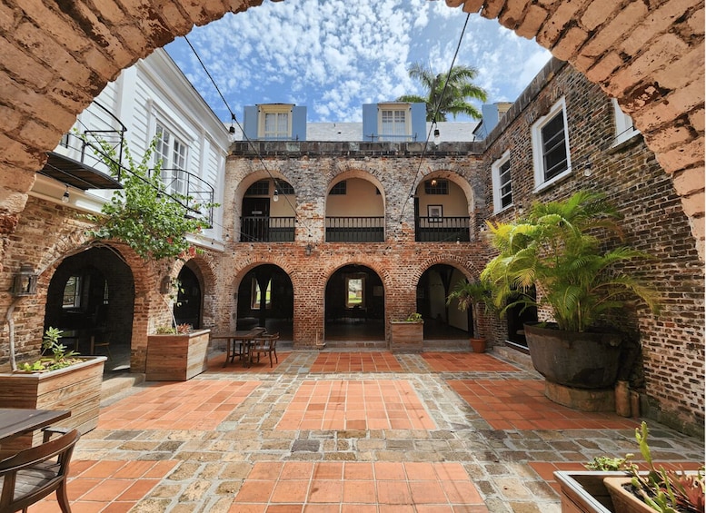 A courtyard with brick arches, a wooden table, and potted plants. 2