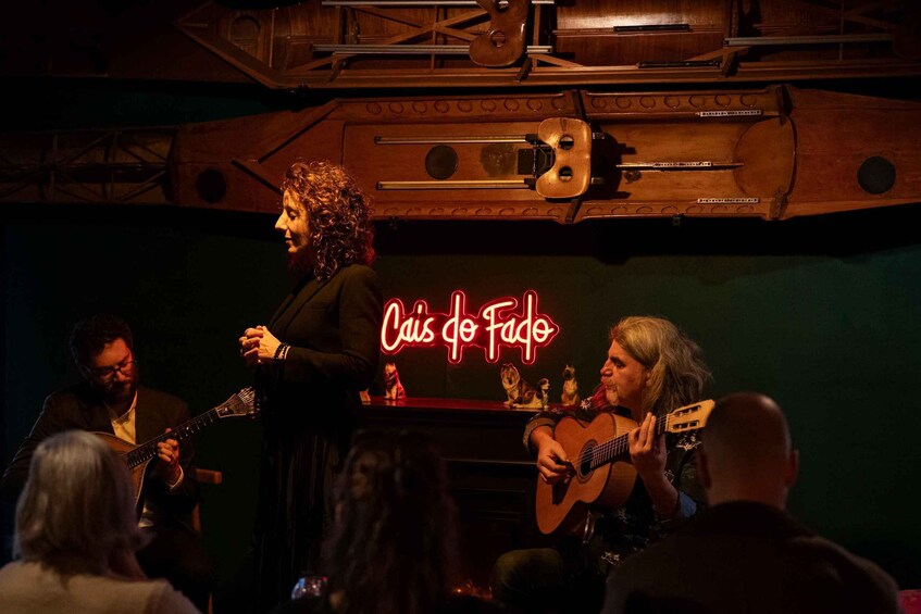 Una banda tocando en el escenario, con un letrero de neón que dice 'Cais do Fado' al fondo. 1