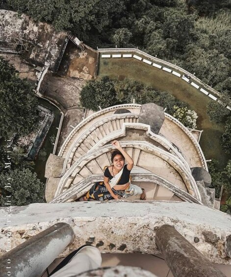 A person sitting on a stone structure with a curved staircase and a railing. 5