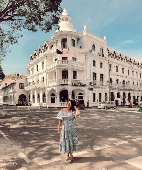 A woman in a floral dress standing in front of a large white building with multiple balconies and a clock tower. 3
