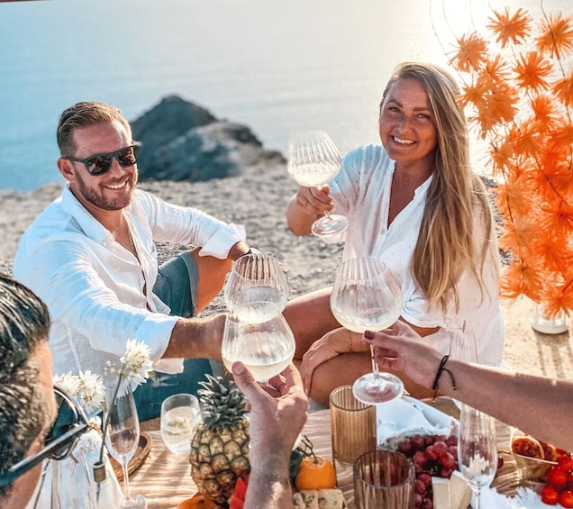 A group of people toasting with wine glasses on a beach with a rocky backdrop. 2