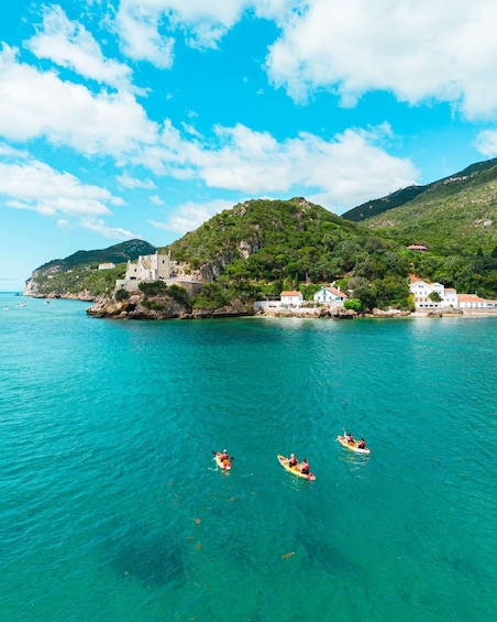 A coastal scene with clear turquoise waters, a small island with buildings, and kayakers in the foreground. 5