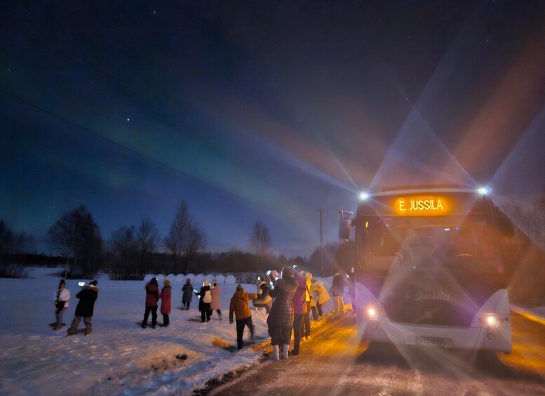 A bus with 'E. JUSSILA' on the side parked on a snowy road with people standing around. 3