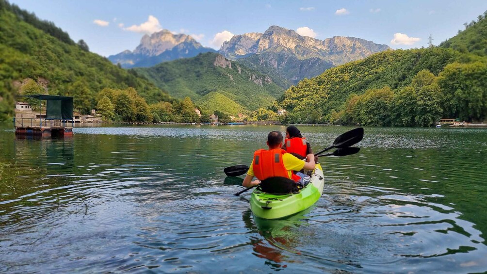 Two people kayaking on a calm lake surrounded by lush green hills and mountains. 1
