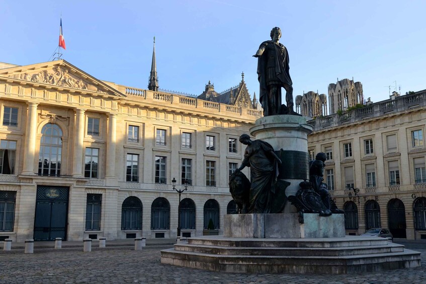 A historical building with classical architecture, a statue of a man, and a flag. 1