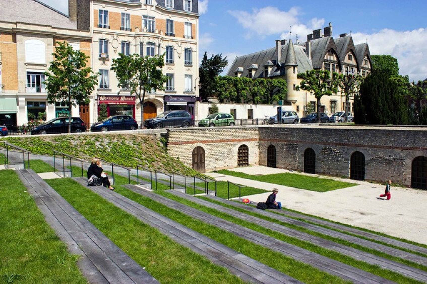 A park with wooden benches, a brick wall, and a building with a turret. 3