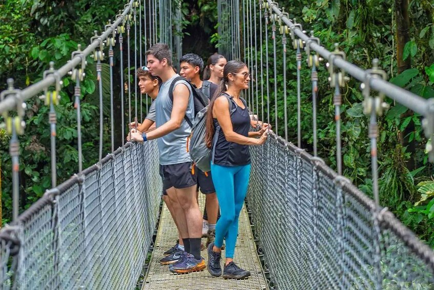 A group of people crossing a suspension bridge surrounded by dense foliage. 2