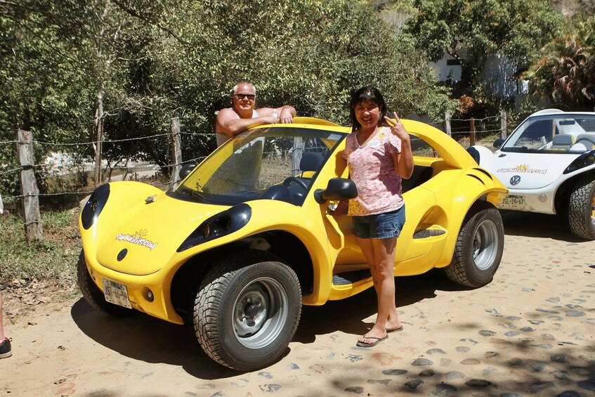 A yellow sports car parked on a dirt road with a fence and trees in the background. 2
