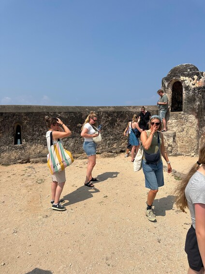 Tourists walking on a dirt path near an old stone wall with a clear sky above. 3