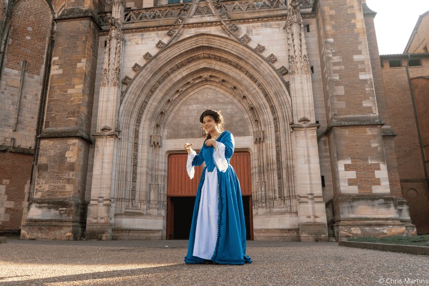 A person in a blue and white dress standing in front of a Gothic-style church with a large arched entrance. 3