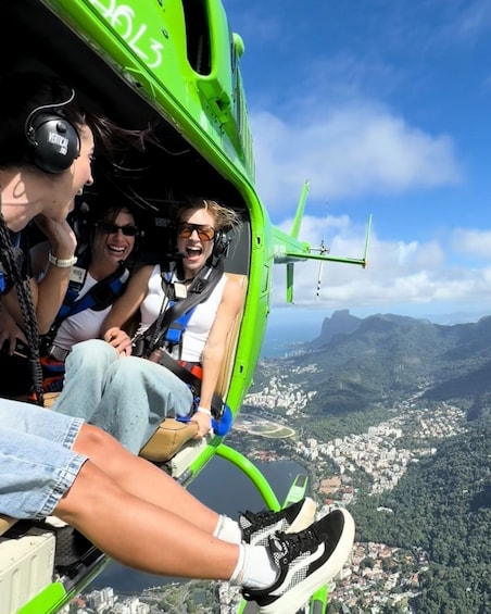 A helicopter with passengers wearing safety harnesses, flying over a city with mountains in the background. 5