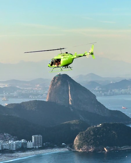 A green helicopter flying near a large mountain and a beach. 2