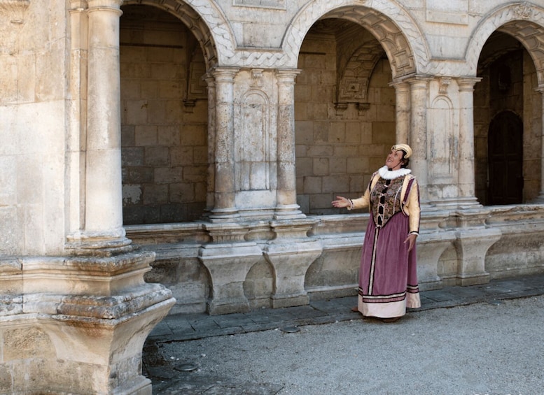 A person in historical costume standing in front of a classical building with arches and columns. 2