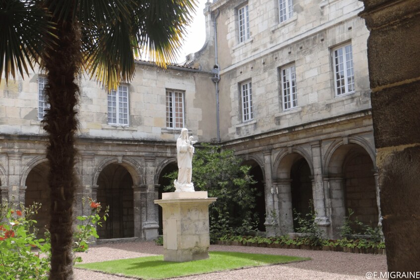 A courtyard with a statue, stone buildings, and a palm tree. 3