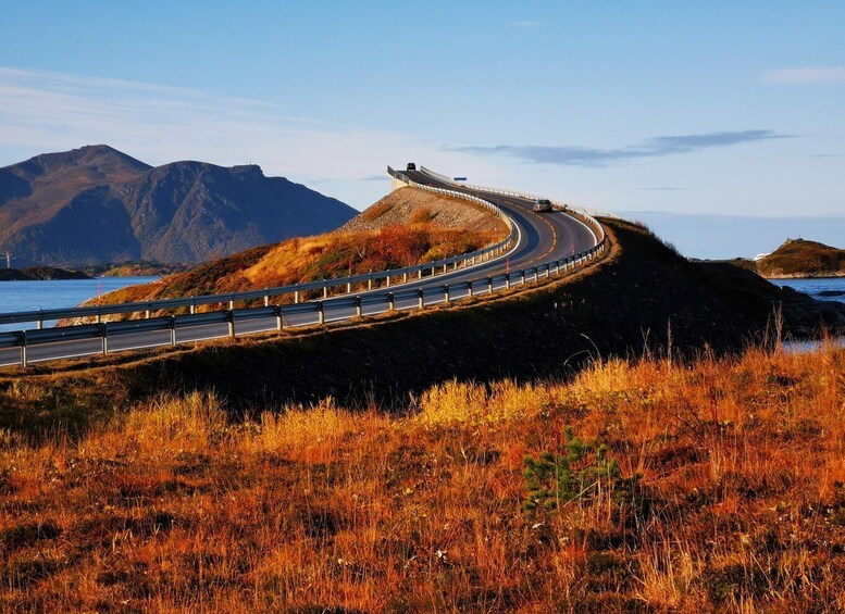A winding road curving along a coastal cliff with autumn foliage and mountains in the background. 3
