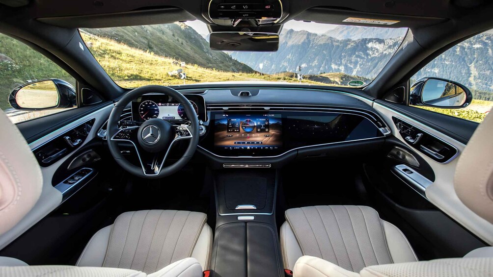 A car's interior with a digital dashboard, steering wheel, and beige seats. 4