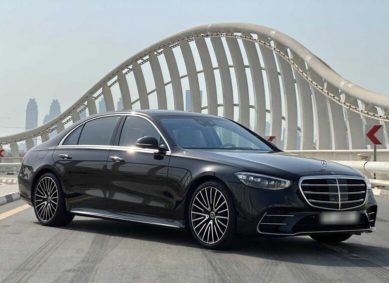 A black Mercedes-Benz sedan parked on a bridge with a modern, curved metal structure in the background. 2