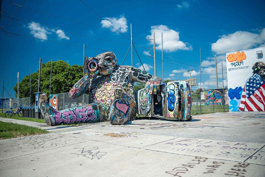 A graffiti-covered sculpture of a bear with a bicycle, surrounded by a fence and a mural. 5