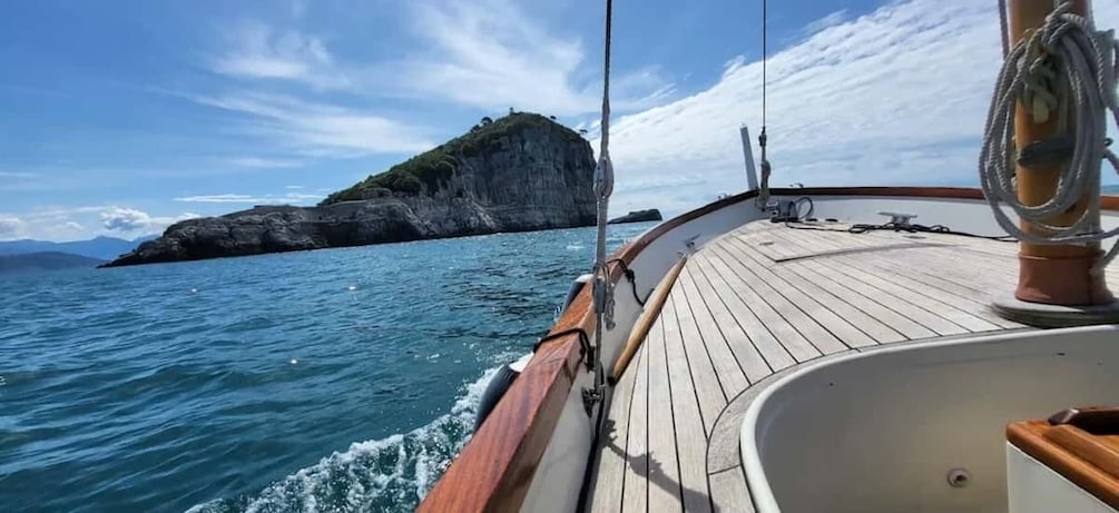 A wooden boat deck with ropes and a view of a rocky island in the distance. 2