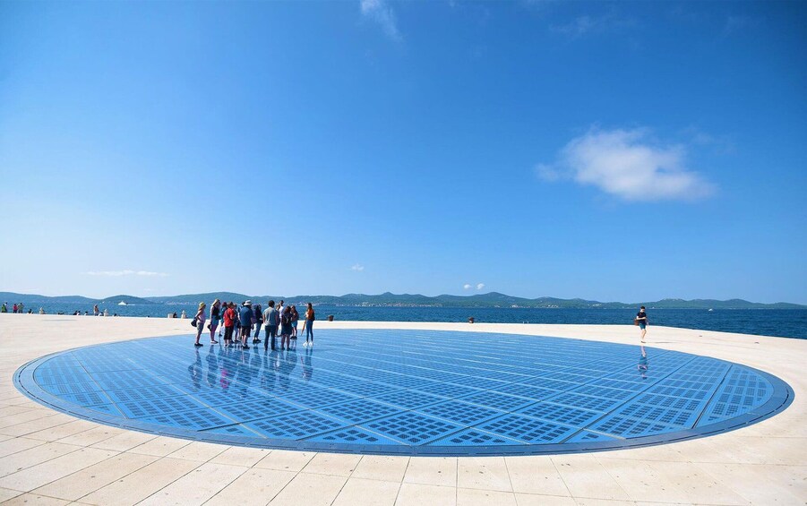 Instalación circular de paneles solares azules rodeada de un grupo de personas en un día soleado. 2