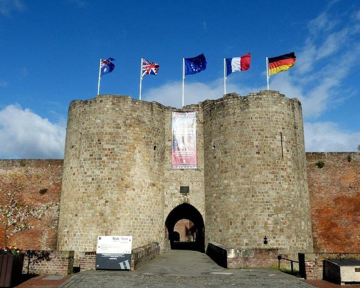 A historic stone gate with flags of the UK, EU, France, and Germany. 2
