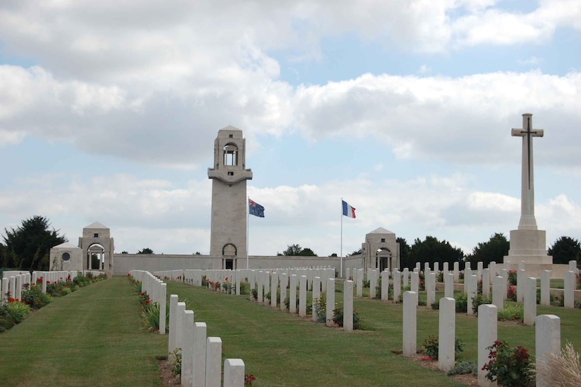A cemetery with white headstones, a central monument, and a tower. 3