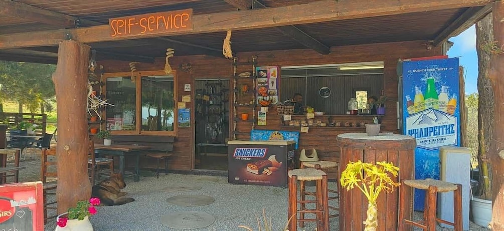 A rustic outdoor café with wooden furniture, a self-service sign, and a Snickers ice cream display. 3