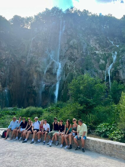 Un grupo de personas sentadas en un saliente con una cascada al fondo. 5