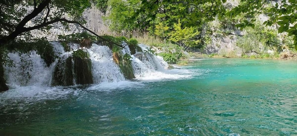 A waterfall cascading into clear turquoise water surrounded by lush greenery. 5
