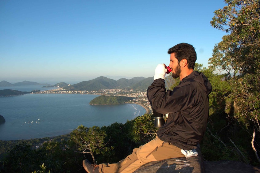 A person sitting on a rock overlooking a coastal landscape with mountains and a town in the distance. 2