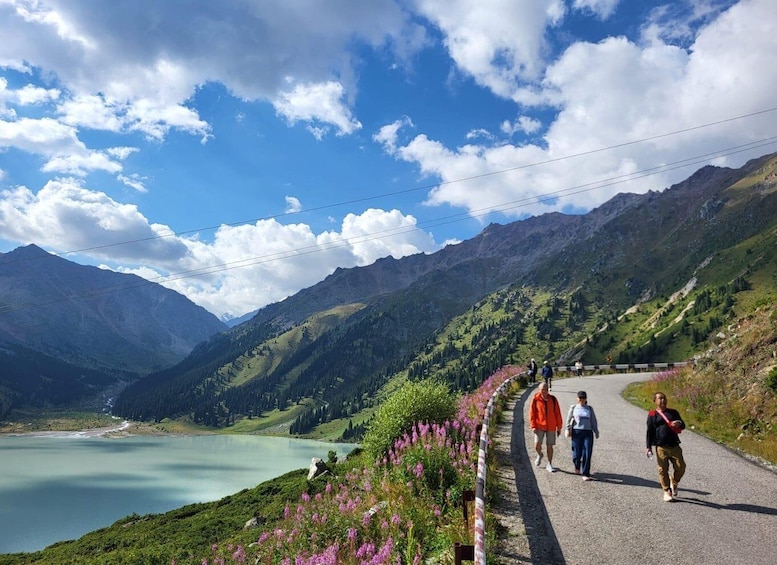 A mountain road with hikers, a lake, and a clear sky. 3