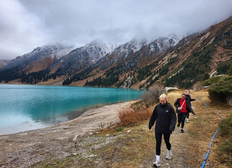 Two people walking along a lakeshore with mountains in the background. 5
