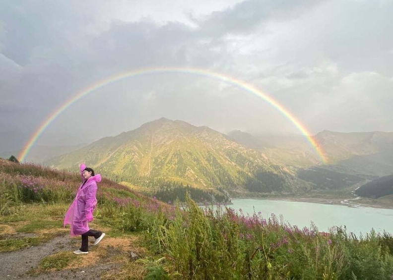 A person in a pink raincoat walking on a path with a rainbow and mountains in the background. 2